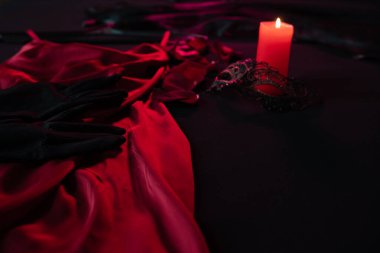 Gül yaprakları, kadın ıvır zıvırları ve kırmızı saten bir elbisenin yanında, koyu renkli bir yatakta mum. Sevgililer Günü 'nde tutkulu bir randevuya hazırlanıyorum. Yakın plan.