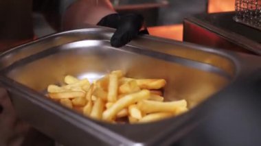 Şefin elleri metal bir kapta patates kızartması ve tuz serpiştiriyor. Fast food restoranlarında yemek pişirmek, yakın çekim.