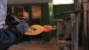Koruyucu eldivenlerdeki ustanın elleri metal maşaları tutar ve onları demir bir boruyla savrulan erimiş cam bir figür haline getirir. Atölyede cam süsleme işlemi, yakın plan.