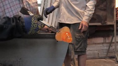 Koruyucu eldivenlerdeki ustanın elleri metal maşaları tutar ve onları demir bir boruyla savrulan erimiş cam bir figür haline getirir. Atölyede cam süsleme işlemi, yakın plan.