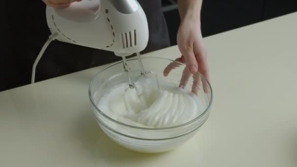 手は白いミキサーとガラスの透明なディーププレートを保持し クリームのための砂糖で卵白をホイップします スローモの台所のレシピに従って調理のプロセス — ストック動画