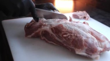 Siyah lateks eldivenli eller, parlak sarı ışığın arka planındaki damarları keserek filmi bir et parçasından ayırdı. Domuz doğrama işlemi, yakın plan.