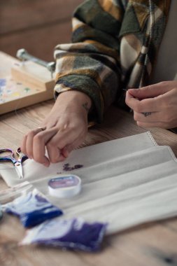 Efendinin eli, bileziğin gelecekteki ürünü için konteynırdan mavi boncukları ipliğe bağlar. Boncuk dokuma işlemi, dikey olarak.