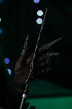 Avucunun içinde siyah tahta bir değnek vardı. Siyah pençeli bir eldiven takıyordu. Koyu yeşil arkaplanda sihirli bir obje parlayan bokeh, dikey yakın plan