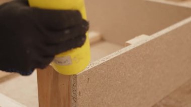 İşçi el, sarı bir kavanozu tutar ve PVA yapıştırıcısını mobilya yapmak için tahta talaş tahtasına yapıştırır. Üretimde süreç, yakın çekim yavaş