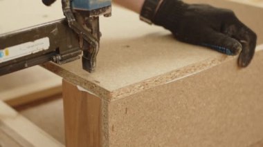 Bir işçi eli, ağır çekimin yakın çekimini bir parça talaş zımbasıyla birbirine bağlar. Mobilya üretme süreci