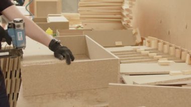 Bir işçi eli, ağır çekimin yakın çekimini bir parça talaş zımbasıyla birbirine bağlar. Mobilya üretme süreci