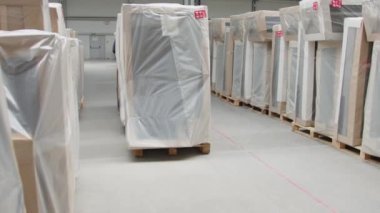 Beyaz polietilen ile paketlenmiş mobilyalar diğer paketler arasında çimlerin işlendiği deponun içine taşınıyor. Büyük bir yığın fabrika ürünü, yavaş.