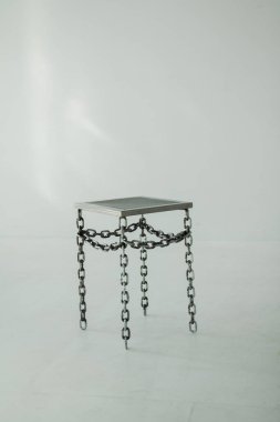 Zincirli bacaklı metal bir sandalye düz beyaz bir arka planda durur. Bir fotoğraf stüdyosunda çekim için sahne donanımı, dikey çerçeve izole