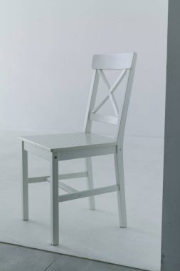 Sırtı olan beyaz bir sandalye, bir ışık siklonamasının sade arka planında duruyor. Minimalist fotoğraf stüdyosu dekoru, dikey çerçeve, izole nesne