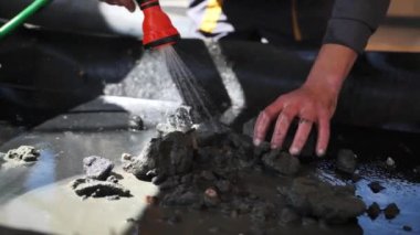 Bir işçi elleri, kazı alanında çıkarılan kehribar çakıl taşlarını tutar ve onları bir su akıntısı ile yerden siler. Yarı değerli kaya madenciliği, yavaş çekimin yakın çekimi