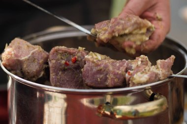 Bir el, salamura edilmiş bir çürük eti parlak metal bir tepside duran şişlere bağlıyor. Barbekü pişirme, yakın plan.