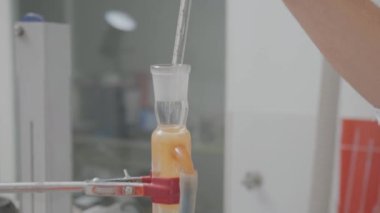 Pipetten bir damla reaktör ocağın üstündeki bir tüpe ekleniyor. Laboratuvarda kimyasal deneyler, yakın çekim, düz sürüş.