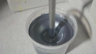 Endüstriyel bir alet, vernik ve boya üretiminde şeffaf bir kapta gümüş metalik boya karıştırıyor. Enamel yapımı, yüzey kaplaması, yakın plan.