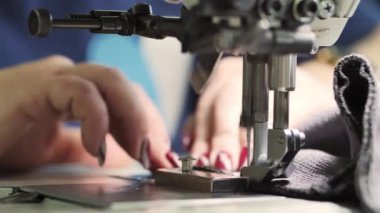 Terzinin elleri dikiş makinesinin iğnesinin altına kumaşı itiyor, dikişleri dikiyor. Üretimde tekstil üretimi süreci, yavaş çekim