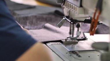 Terzinin elleri dikiş makinesinin iğnesinin altına kumaşı itiyor, dikişleri dikiyor. Üretimde tekstil üretimi süreci, yavaş çekim