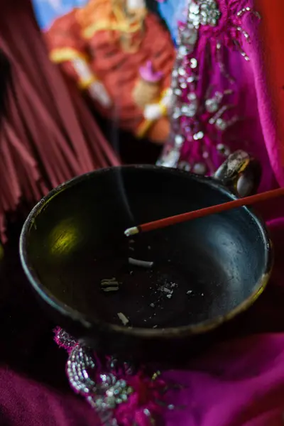 stock image A red incense stick smolders on a stand in a thin trickle of smoke in slow-mo on a crimson background with golden bokeh that fades. Hindu ritual of offering to the gods, close-up, macro