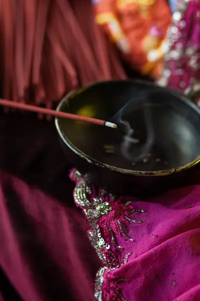 stock image A red incense stick smolders on a stand in a thin trickle of smoke in slow-mo on a crimson background with golden bokeh that fades. Hindu ritual of offering to the gods, close-up, macro