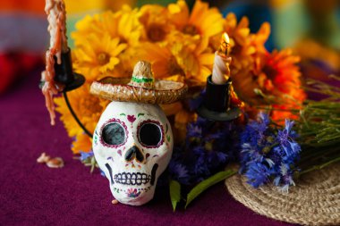Küçük bir Lambrero 'da kafatası şeklinde boyanmış bir heykel, yanan mumların yanındaki çiçeklerle süslenir. Meksika Ölüler Günü 'nün sembolleri. Renkli, parlak bir arka planda.