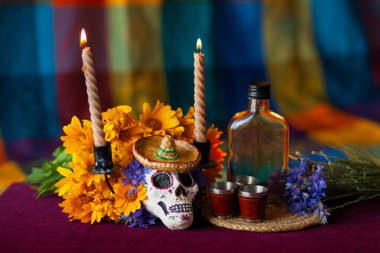 Küçük bir Lambrero 'da kafatası şeklinde boyanmış bir heykel, yanan mumların yanındaki çiçeklerle süslenir. Meksika Ölüler Günü 'nün sembolleri. Renkli, parlak bir arka planda.