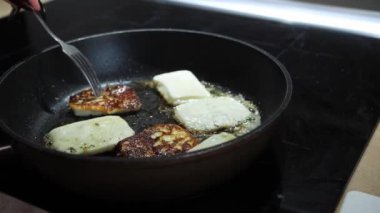 Halloumi peyniri dilimleri tereyağında tavada kızartılır ve el onları bir çatalla çevirir. Ev yapımı kahvaltı hazırlama süreci, yakın plan.