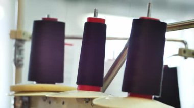 Metal çubuklara dizilmiş üç siyah iplik makarası elbise üretiminde bir dikiş makinesinde dönüyor. Fabrikada teknik işlem, yakın plan.