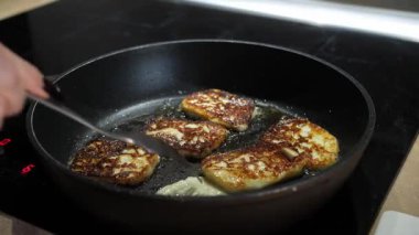 Halloumi peyniri dilimleri tereyağında tavada kızartılır ve el onları bir çatalla çevirir. Ev yapımı kahvaltı hazırlama süreci, yakın plan.