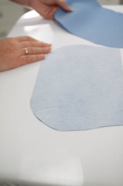 Terzinin elleri astar için kesilmiş mavi kumaş parçalarını tutuyor. Giysi yapma süreci, el dikimi dikey dikey.