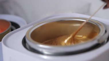 Tüy dökücü ustasının eli, sıcak metal bir kapta eritilmiş altın balmumu karışımını ahşap bir spatulayla karıştırır. Güzellik prosedürü için hazırlık, kozmetoloji yakın çekim