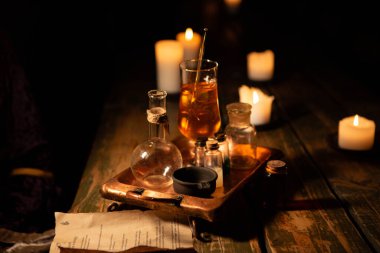 Ahşap bir masanın arka planına karşı bir kokteyl hazırlamak ve mum yakmak için mataralar, bardaklar ve simya kapları antika metal bir tepsiye konur. Yaratıcı bir içki servisi. 