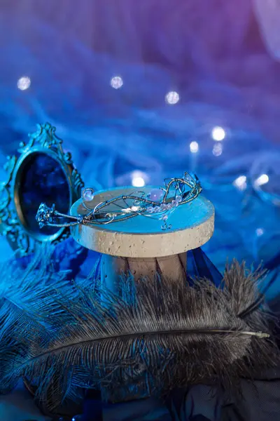 İşlenmiş demir çerçeveli eski bir ayna, parlak mavi bir arka planda, bir çelengin ışıldayan ışıkları arasında devekuşu tüylerinin yanında durur. Büyülü atmosfer, dikey yakın çekim