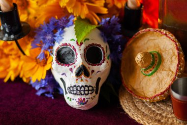 Küçük bir Lambrero 'da kafatası şeklinde boyanmış bir heykel, yanan mumların yanındaki çiçeklerle süslenir. Meksika Ölüler Günü 'nün sembolleri. Renkli, parlak bir arka planda.