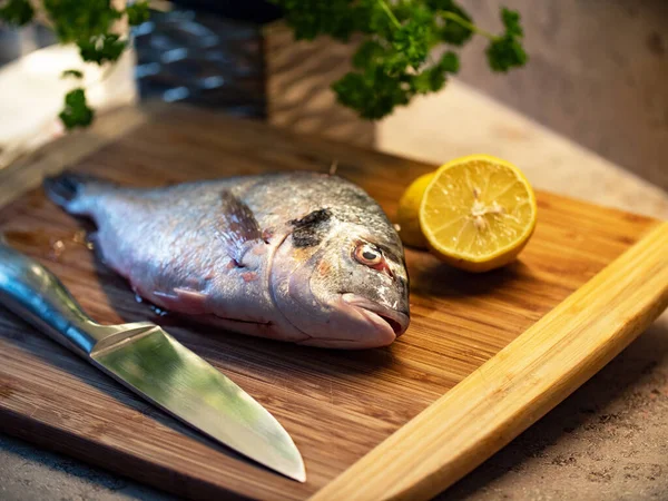 厨房里的生金头鱼 特写镀金鱼在厨房的板子上 鱼旁边有一把半柑橘 健康的海洋食品 — 图库照片