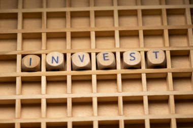 Invest. Wooden dice arranged in a box, to the word Invest. Stock Market, savings and banks. clipart