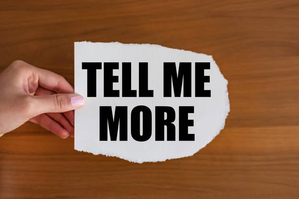 Tell me more. Woman hand holds a piece of paper with a note, tell me more. , Feedback, advice, communication, evidence, education, asking and request.