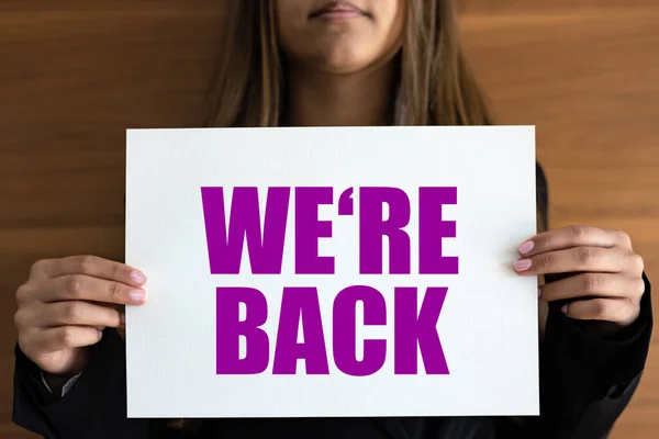 We are back. Woman holds a white page with purple text. New business, shop, retail place, marketing, opening event, beginnins and store concept.