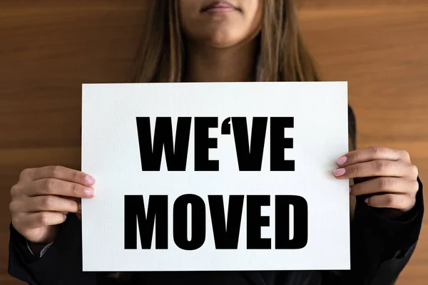 We have moved. Woman holds a white page with orange text. Information sign, new business, location, relocate and new address.