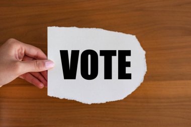 Vote - close up text on the slip. Woman hand holds a piece of paper with text.  clipart