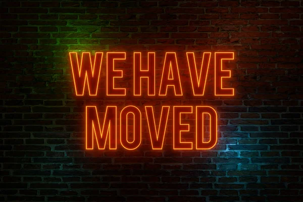We have moved, neon sign. Brick wall at night with the text \
