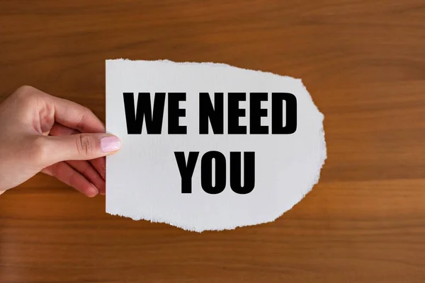 We need you - close up text on the slip. Woman hand holds a piece of paper with text. Recruitment, searching, job opportunity, hiring, team, employment and labour.