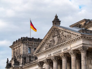 Berlin, Almanya - 9 Ağustos 2021: Bulutlu bir günde Alman Bundestag 'ının merkezi olan ünlü Reichstag binasının yakın çekimi. Alman bayrağı bir kule.