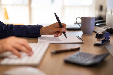 Muhasebeci hesap makinesine el yazıları yazar ve bir sayfaya notlar yazar. Klavyeli, hesap makineli ve ofis aletli bir masa. Kadın katipler tuş takımına el yazıları yazarlar ve diğer el de notlar yazar..