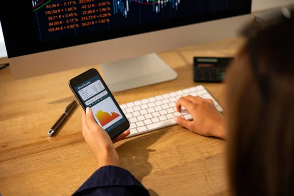 Stock market crash. Woman's hand holds a mobile phone. Dropping stock chart on the screen. PC monitor in the background. Stock market, crisis, financial advisor, loosing money and trading concept.