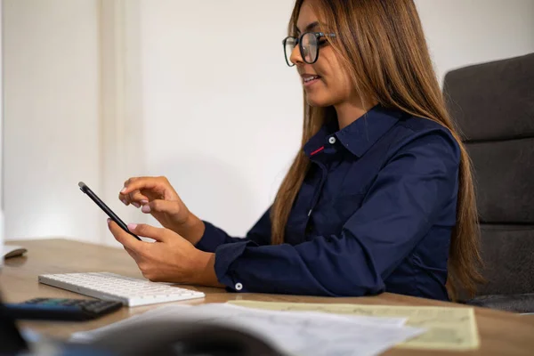 Businesswoman with glasses sits at the desk and types on the cell phone. Back office, business, file clerk, office assistance, work and management.