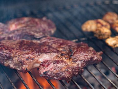 Barbeküde ızgara biftek. Izgara bifteğe yakın çekim. Et dışarıda kavrulmuş durumda. Kömür ve ateş bifteğin altında parlıyor. Yazın barbekü..