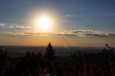 Feldberg 'in Hessen, Almanya' daki dağının manzarası. Ön planda çalılar ve çalılar var. Arkaplanda tepeler ve bulutlarla birlikte geniş bir manzara var. Gün batımında geniş görüş Feldberg.