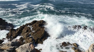 Hermanus, Güney Afrika Ağustos 2020: Atlantik dalgaları karanlık taşların uçurumuna çarpıyor ve su sıçrıyor. Hermanus 'ta zorlu Atlantik kıyıları