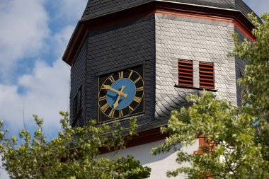 Kilisenin saati çatı kiremitleriyle çevrili. Kilise kulesini saatle kapatın. Mavi ve altın renkli saat yüzlü kadim bir saat. Mavi gökyüzü ve az bulutla güneşli bir gün..