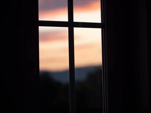 Close-up of silhouette of a window with blurred sunset as background. The middle of the window appears like a cross.