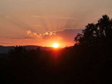 Gün batımı ve bulutlar, siluet dağları ve ağaç. Bulutlar, güneşin alacakaranlıkta gizlenmiş dramatik Sunset Hochtaunus, Hessen, Almanya. Güneş batıyor ve bulutların arkasında. Gökyüzü parlak turuncu bir ışıkla parlıyor..